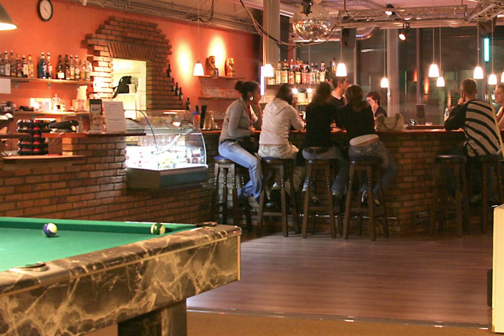 Gäste an der Bar-Theke mit Backsteinwand und Getränkeregal
