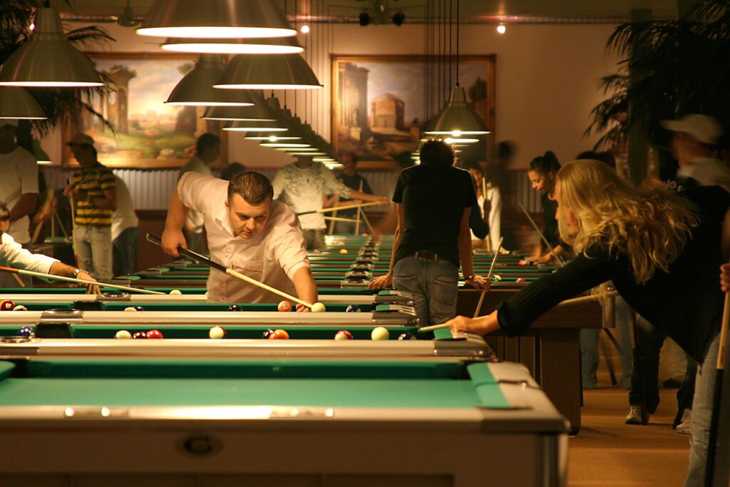 Spieler und Spielerinnen an einer Reihe von Pooltischen am Abend
